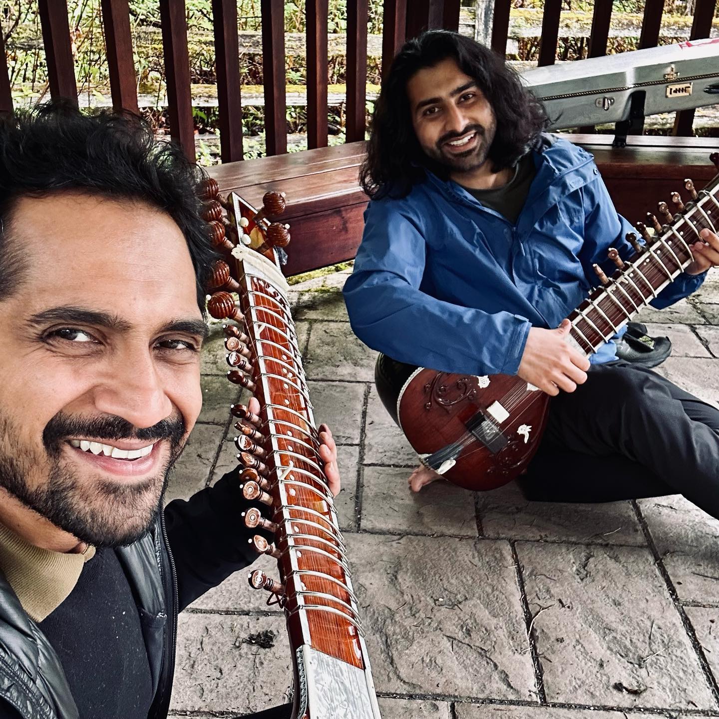 Two sitar players sitting outdoors